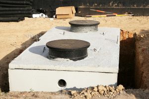 A concrete septic tank is shown in a freshly dug hole, ready for installation.