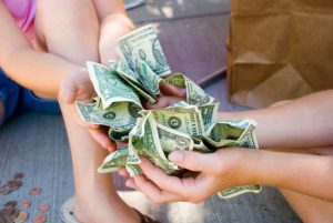 Two pairs of hands hold crumpled dollar bills.