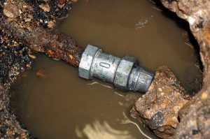 Leaking pipe repair, with a metal coupling joining two sections of rusted pipe.