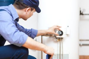 A man in uniform kneels to adjust a water heater.