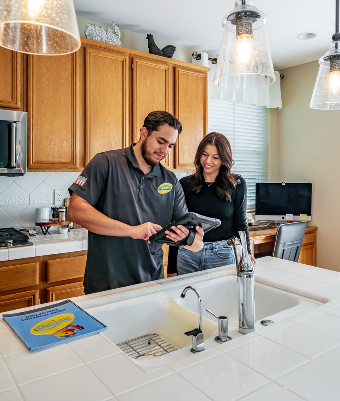 Service technician showing tablet to a woman homeowner in a kitchen by a white tile sink