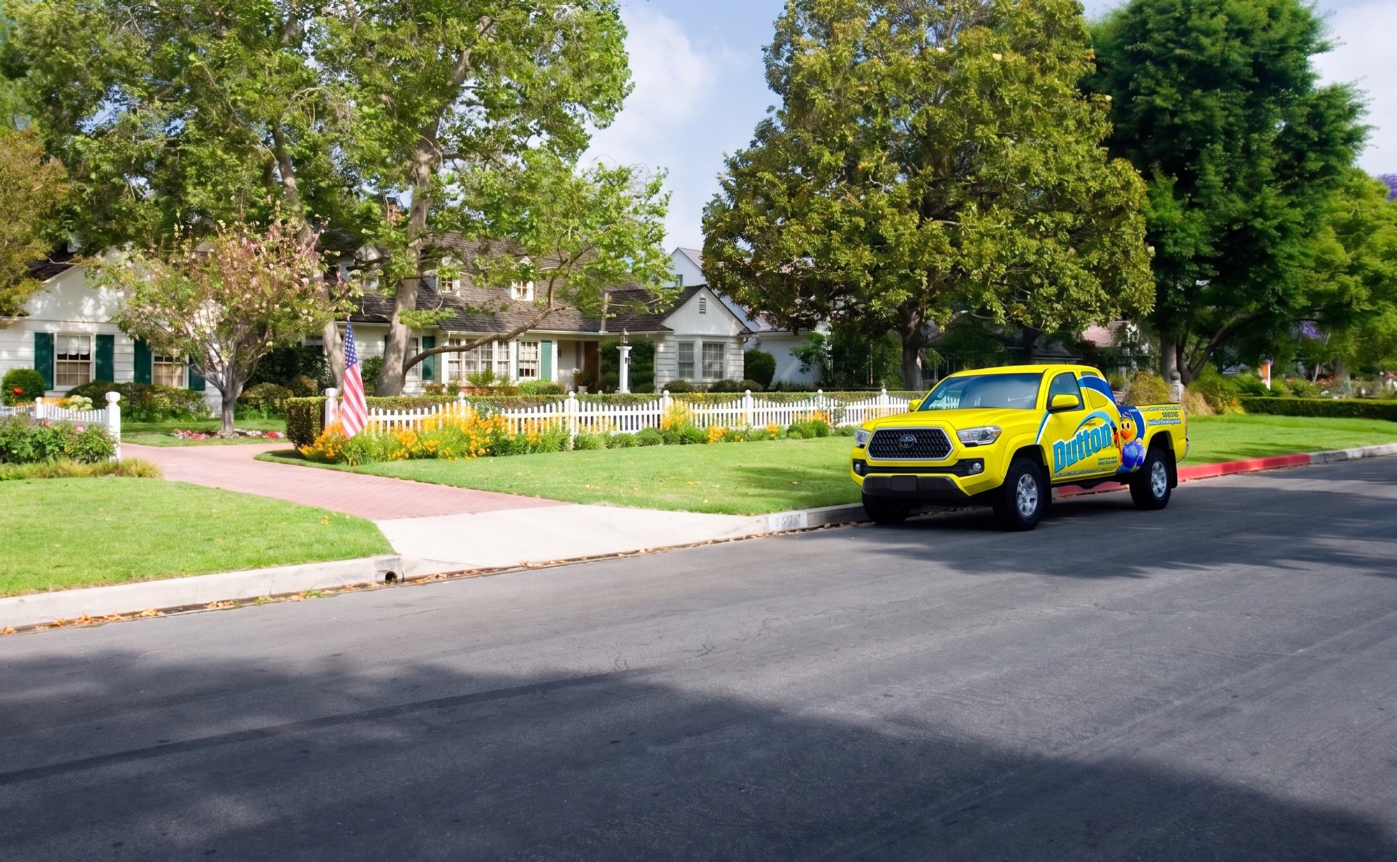 Suburban house with white picket fence, American flag, manicured lawn and yellow branded service pickup parked curbside