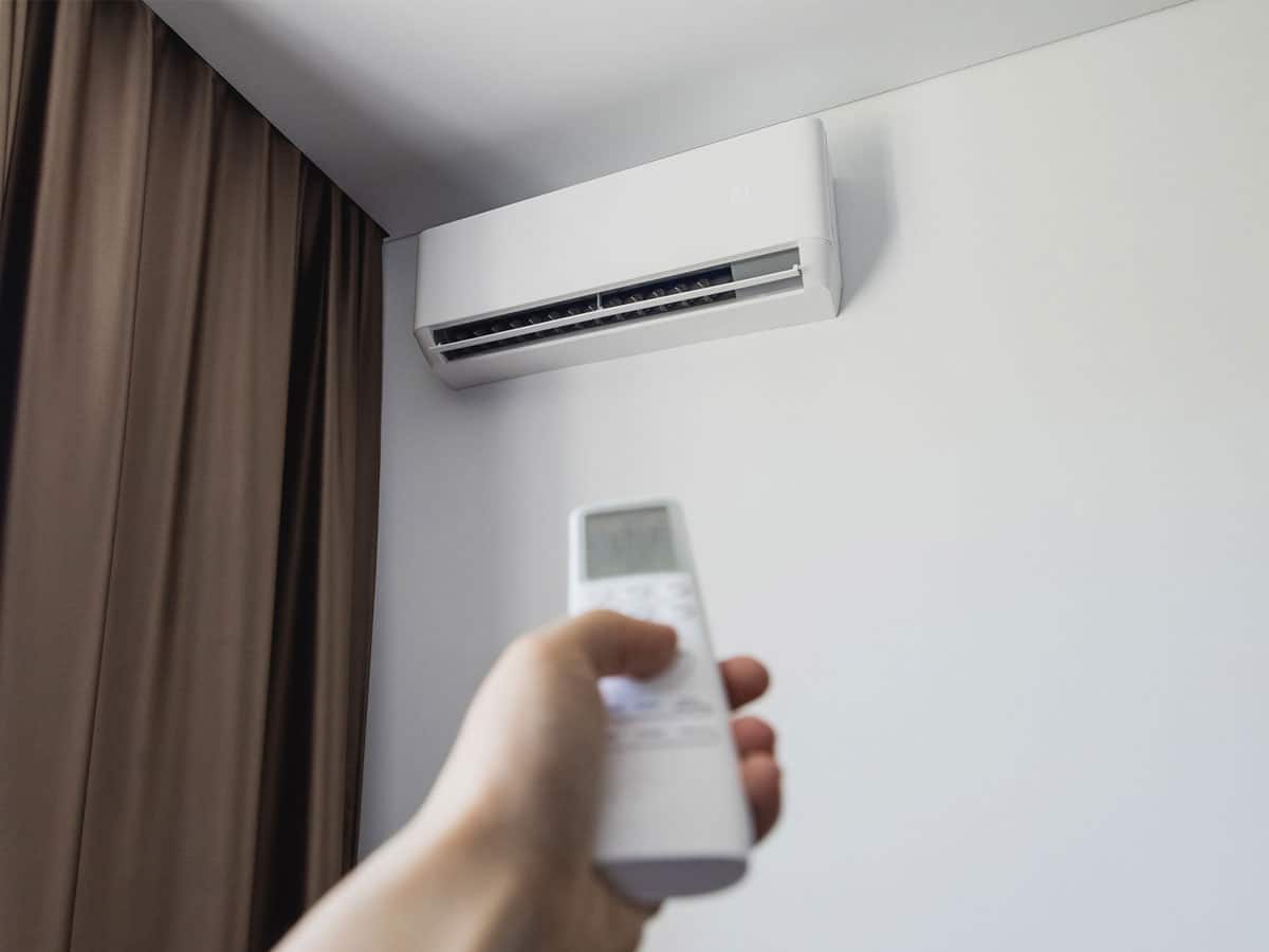 Person pointing a remote at a wall-mounted split air conditioner near brown curtains