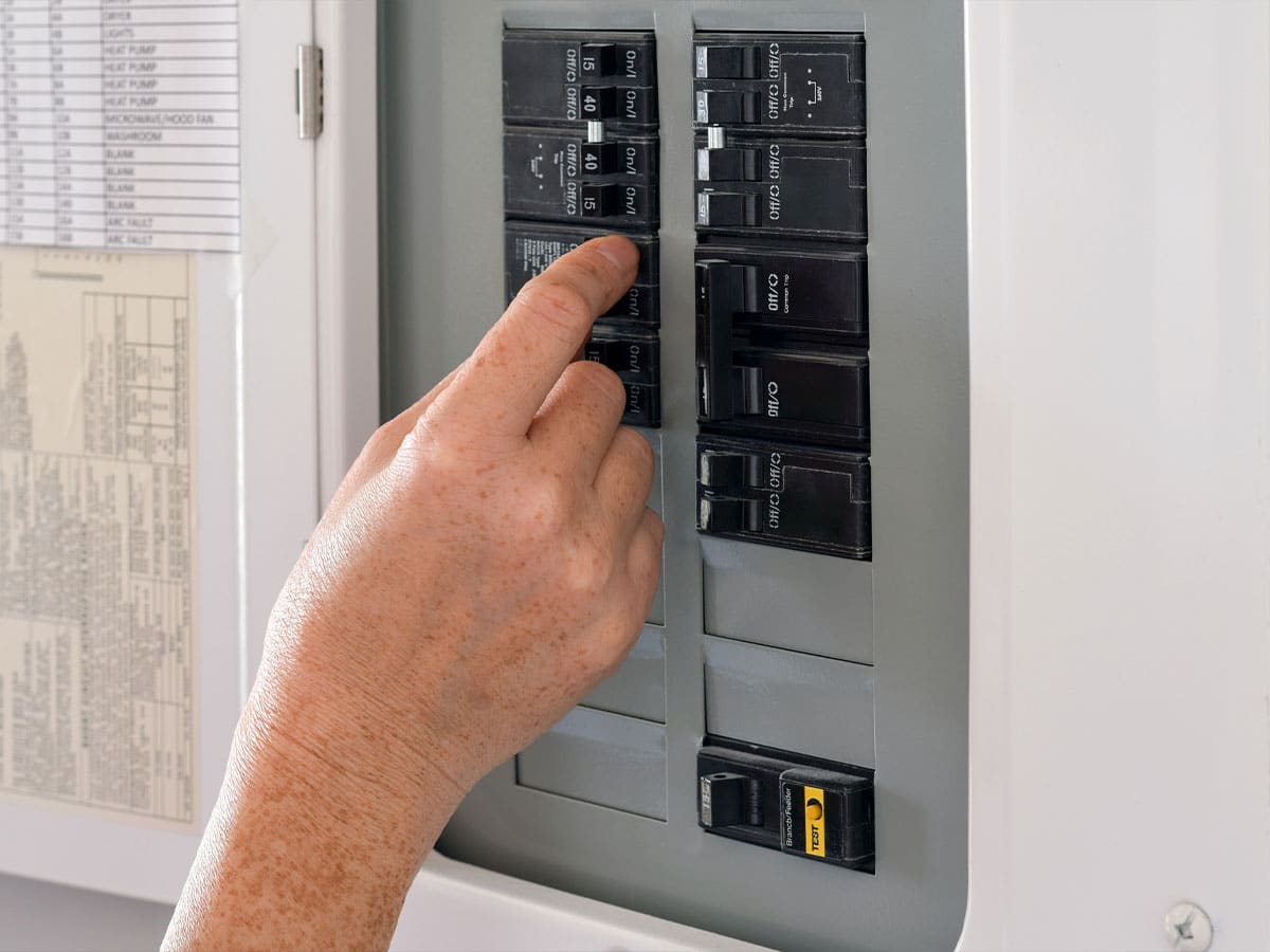 A person flipping a circuit breaker in a residential electrical panel