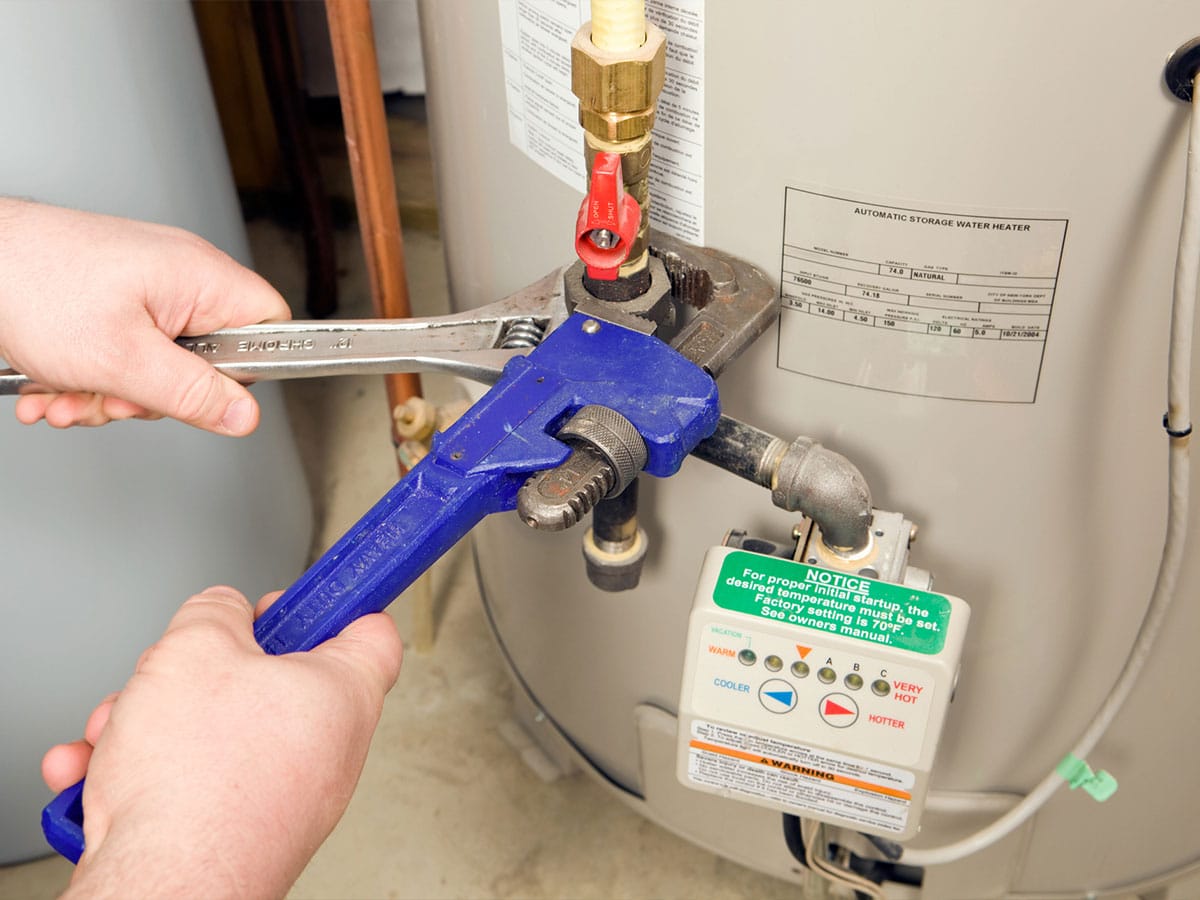 Hands using blue pipe wrench and adjustable wrench to tighten valve on a residential water heater