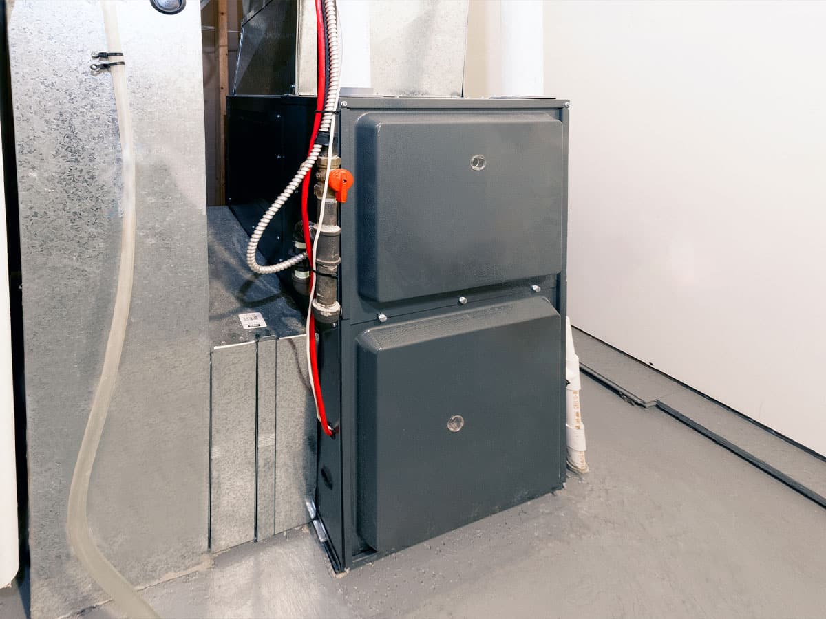 Basement HVAC furnace and air handler with ductwork, red condensate line, and gray metal panels on concrete floor