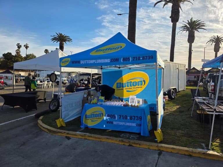 Dutton Plumbing blue promotional tent and table with giveaways at outdoor community event under palm trees