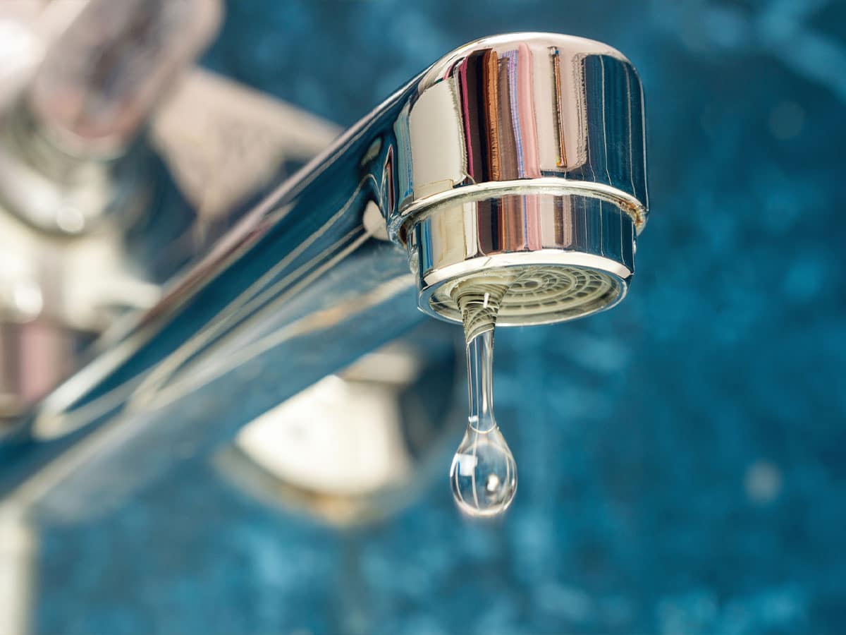 Close-up of a chrome faucet with a single water droplet forming at the spout against a blue background