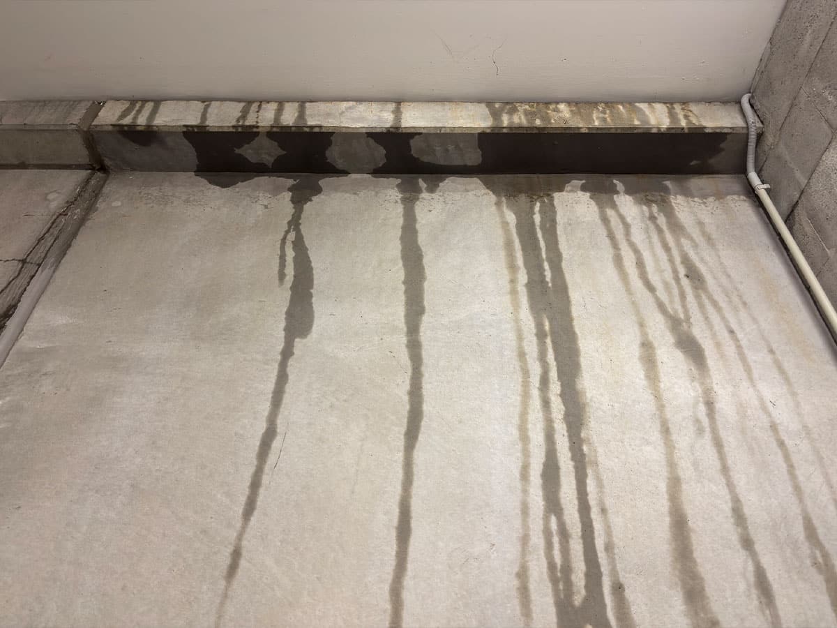 Concrete wall with vertical water stains from ceiling leak and visible conduit pipe