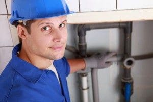 Plumber in blue hard hat inspecting household pipes in a utility room