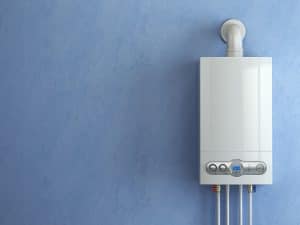 White tankless water heater mounted on blue wall with silver control knobs and three connected pipes.