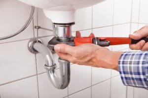 A plumber tightening a chrome P-trap under a bathroom sink with a red pipe wrench