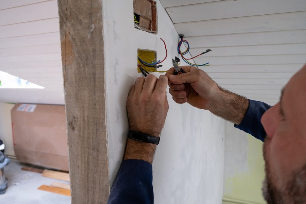 An electrician using wire cutters to connect electrical wires in a wall junction box during home renovation.