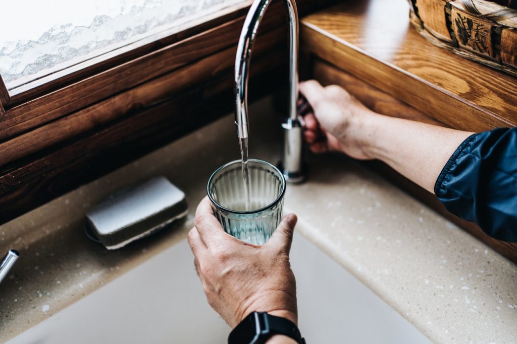 Person filling a glass under a kitchen faucet with tap water