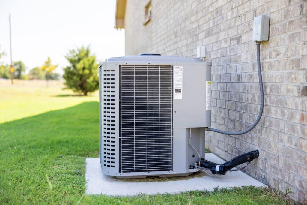 Outdoor central air conditioner condenser unit on concrete pad beside brick house and green lawn