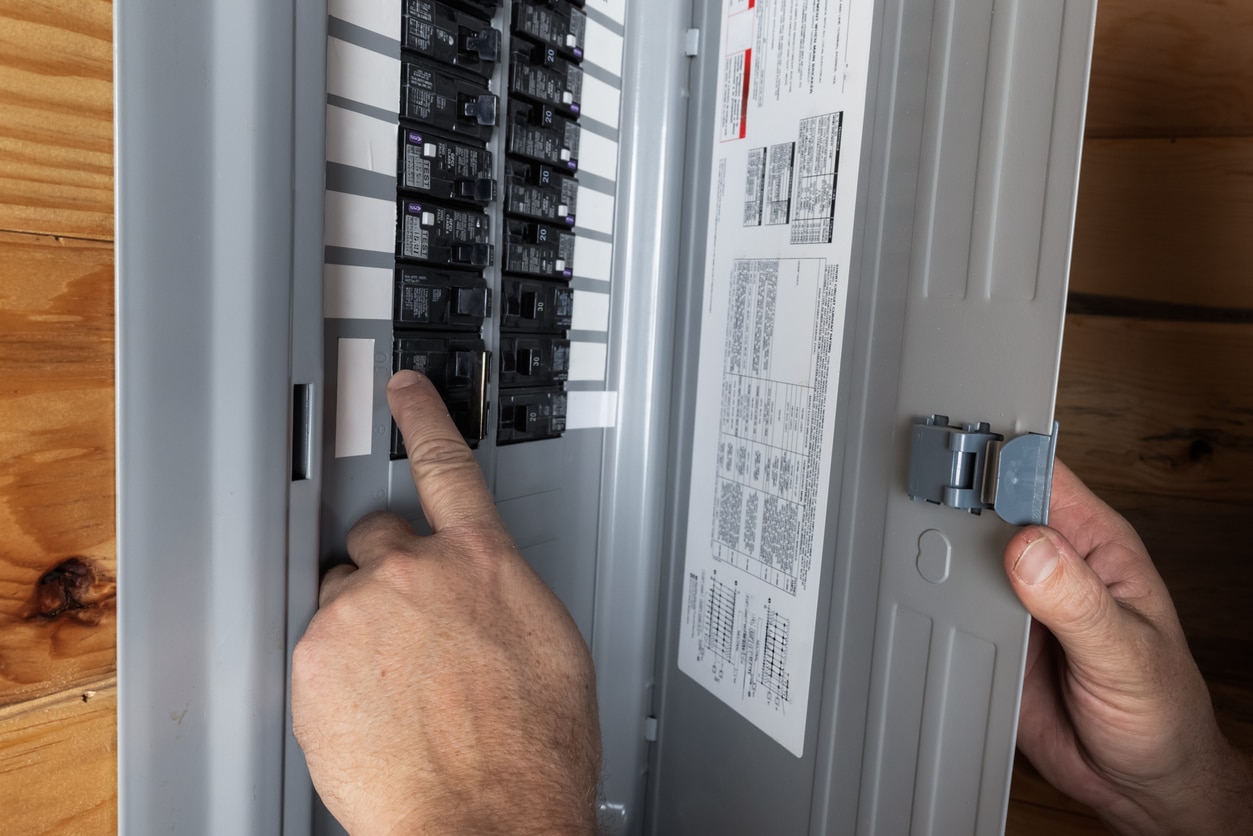 A person inspecting a home's electrical breaker panel, finger pointing at a circuit breaker switch.