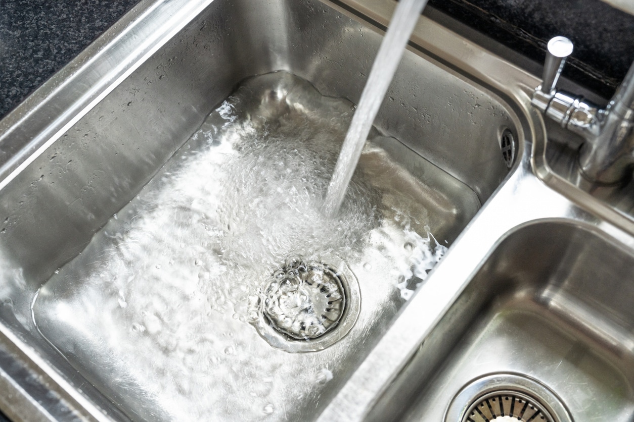 Stainless steel kitchen sink with running water streaming into the drain of a double-basin sink.