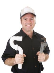 A smiling plumber in cap holding PVC pipe and pipe wrench on white background.