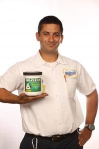 A man in a white polo holding a container of Bio-Clean cleaning product, smiling at camera